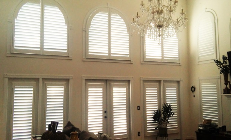 Entertainment room in open concept Bluff City home with plantation shutters on arch windows.