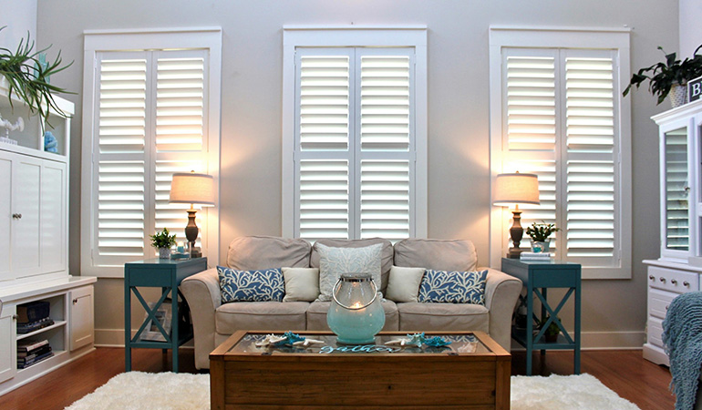 White Polywood shutters on three windows in a white and blue living room