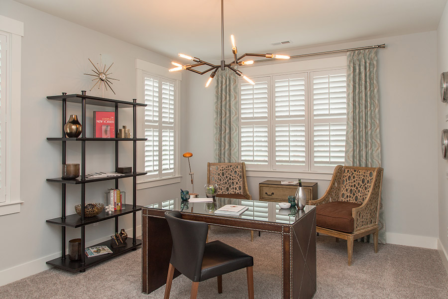 Sage green patterned curtains on white polywood shutters in an office.