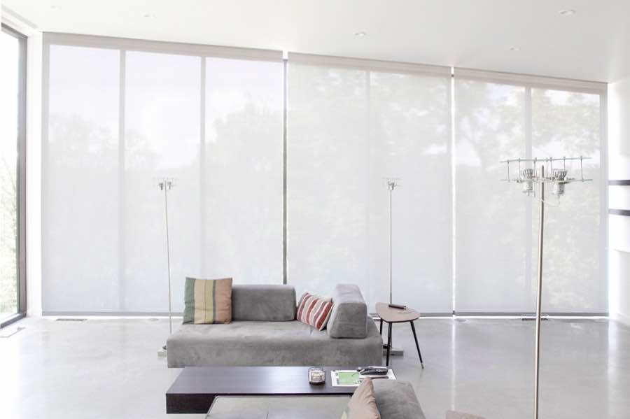 Motorized window shades make controlling natural light effortless in your Bluff City great room. White motorized shades on a wall of tall great room windows