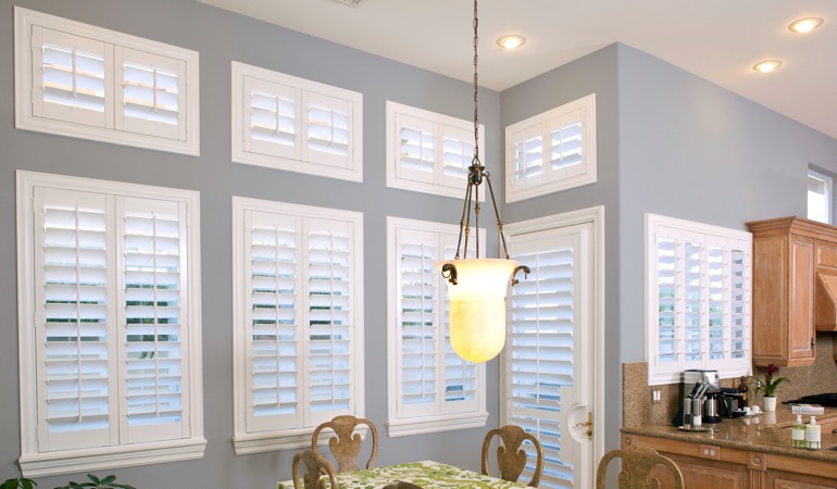 Shutters can fix both sun glare and energy efficiency problems. White plantation shutters in dining room