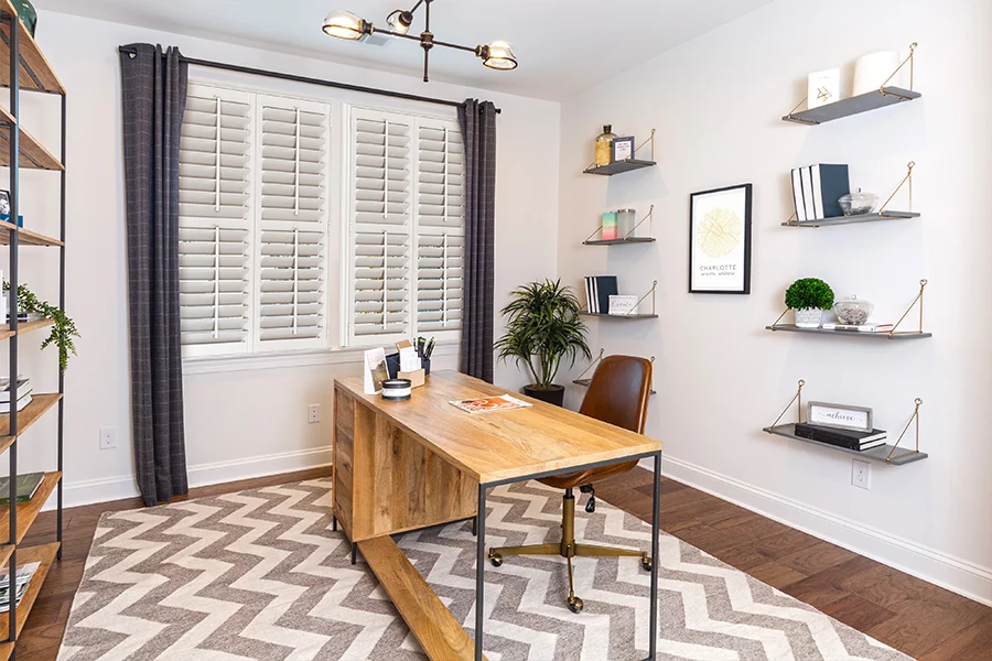 Get the most options for stylish window coverage in your home office when you combine drapes with interior shutters. Polywood shutters with divider rails and gray drapes on a home office window